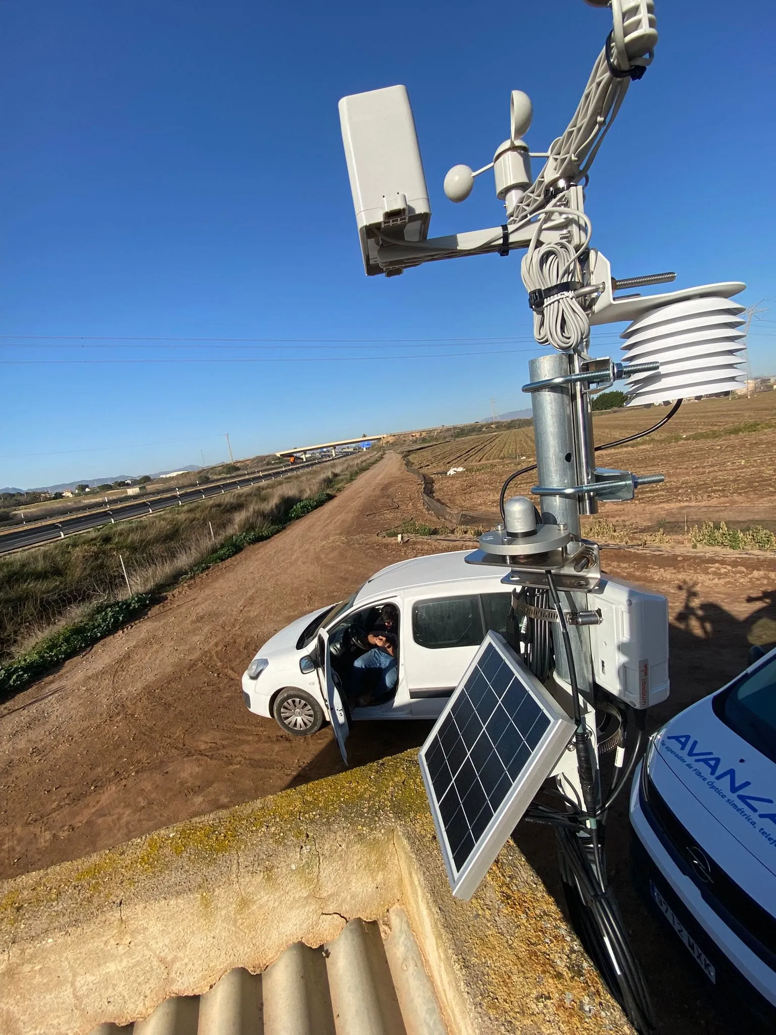 Mástil con cámara de vigilancia y placa solar junto a una furgoneta en obra